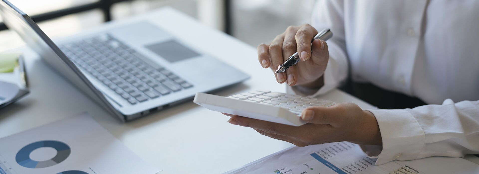Professional calculating asset values beside a laptop and printed financial charts